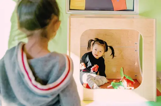 A young learner smiles from inside a Natural Pod Play Cube, creating a cozy + calming space for individual play.
