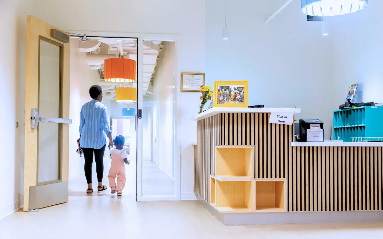 An educator and child walk away from the front desk at the Boston Square Early Learning Center.