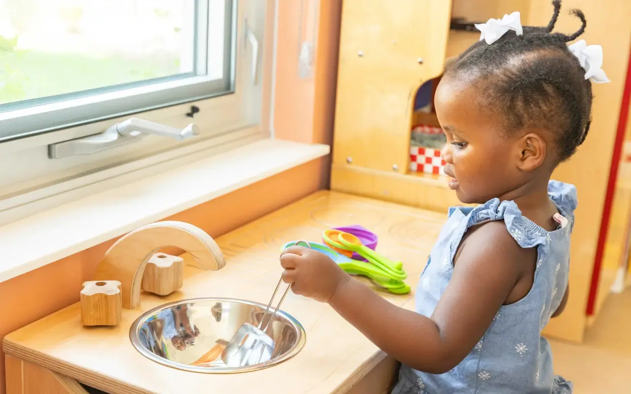 A toddler plays with a Natural Pod play kitchen, with natural light from a large window.