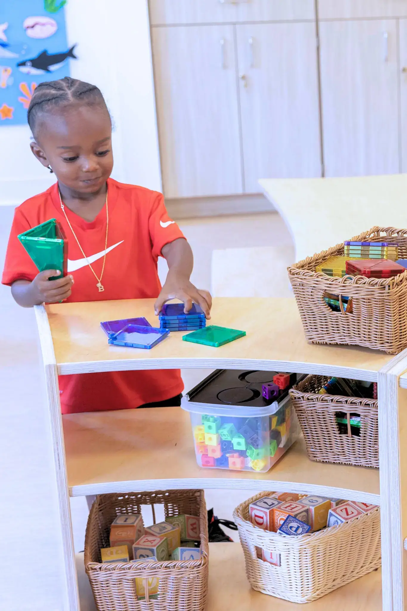 A child plays with magnetic tiles at a Natural Pod Evergreen Shelving unit.