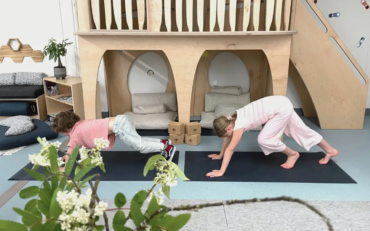Two children do yoga on mats in a room with a Wonder Play Loft and other biophilic design elements.