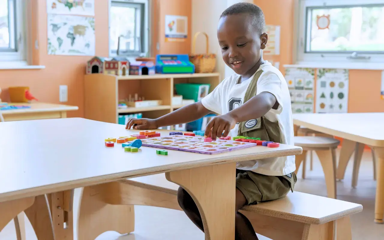 A learner plays a board game at a Natural Pod Reach Table, sitting on a Share Bench.