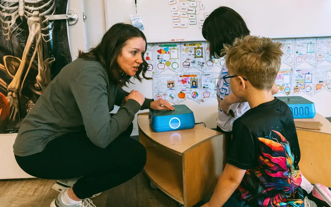Principal Donna Rankin-Anderson crouches by a Natural Pod Evergreen shelf, talking with two students at Thrive Elementary. Principal Donna Rankin-Anderson crouches by a Natural Pod Evergreen shelf, talking with two students at Thrive Elementary.