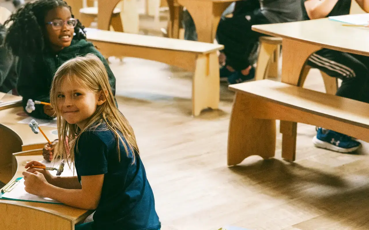 A student smiles while sitting at flexible Evergreen Shelving, with other students using Reach Tables in the Thrive Elementary classroom. A student smiles while sitting at flexible Evergreen Shelving, with other students using Reach Tables in the Thrive Elementary classroom.