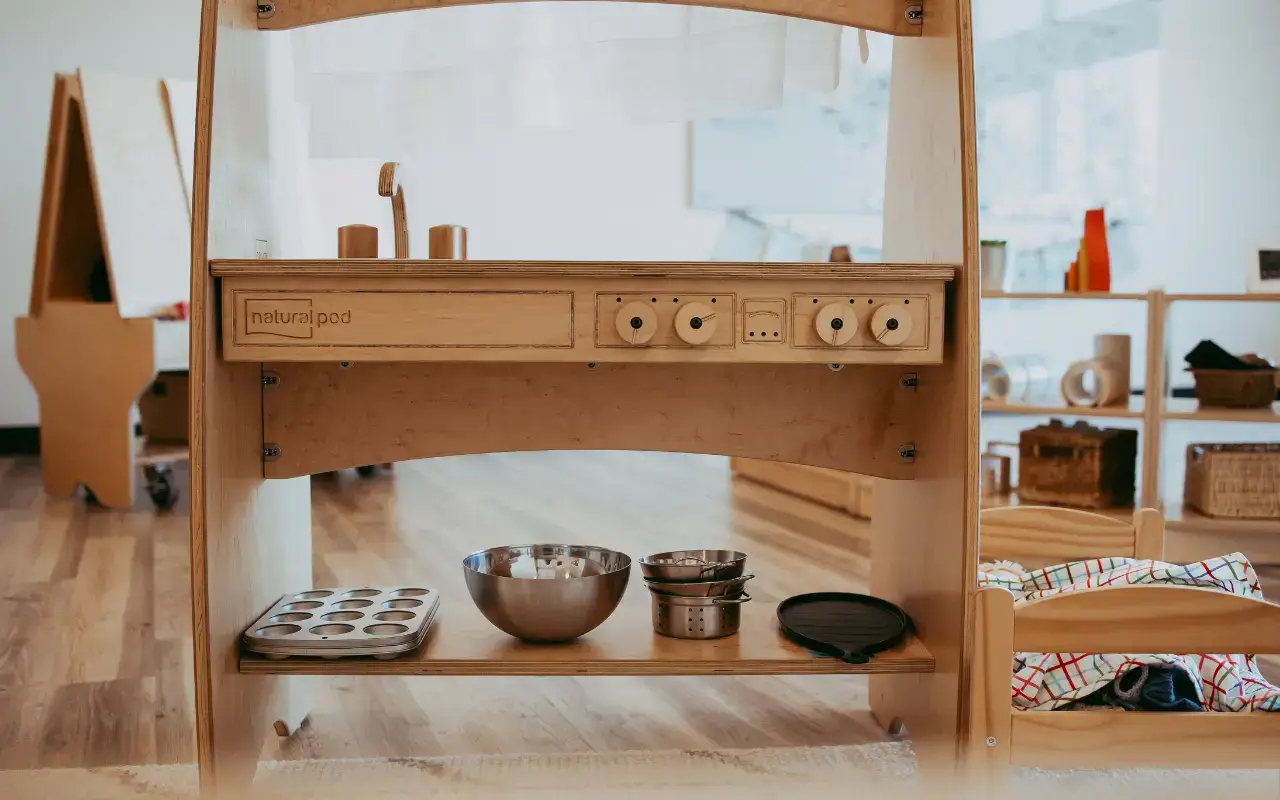 A close-up of a Natural Pod Imagine Play Stand with kitchen items, a piece of wooden preschool furniture.