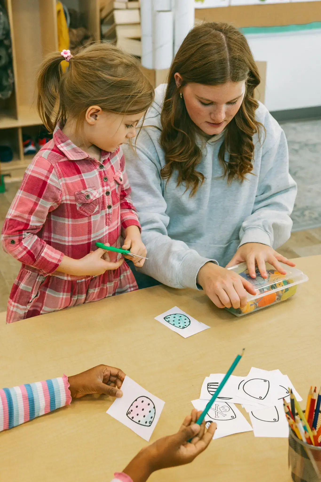 An educator helps a student with a craft activity at a Natural Pod Reach Table in a Thrive Elementary classroom. An educator helps a student with a craft activity at a Natural Pod Reach Table in a Thrive Elementary classroom.
