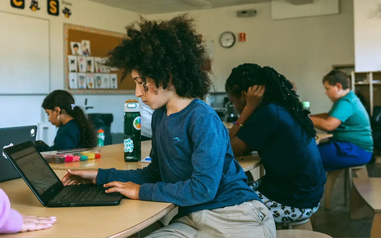 A student with curly hair works on a laptop at a wooden table in a STEM lab at Thrive Elementary. A student with curly hair works on a laptop at a wooden table in a STEM lab at Thrive Elementary.