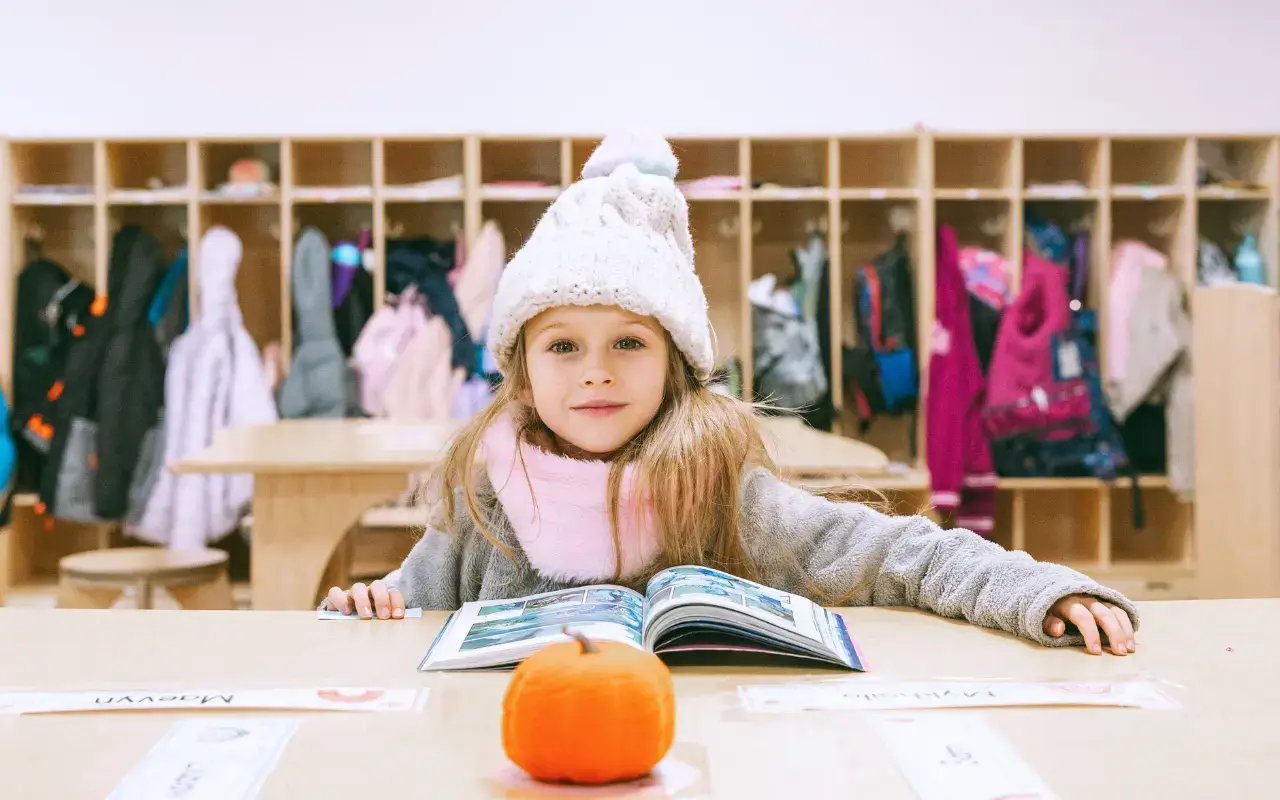 A student in a winter hat sits at a Natural Pod Reach Table reading a book, with classroom cubbies in the background. A student in a winter hat sits at a Natural Pod Reach Table reading a book, with classroom cubbies in the background.