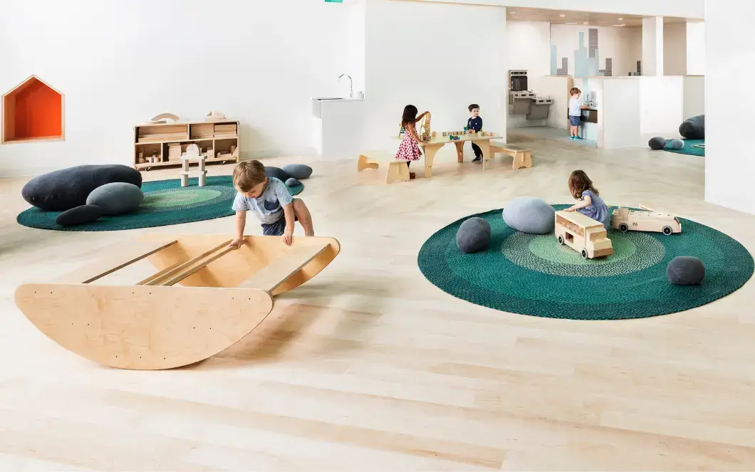 A child balances on an Imagine Rocking Boat and Stairs in a bright early learning space.