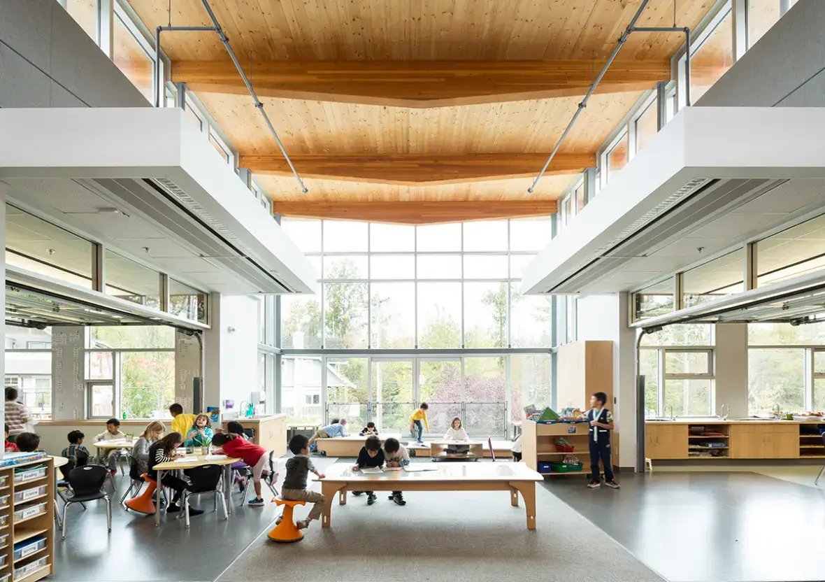 Collaborative wooden Reach Table and active stools in a sunlit, high-ceilinged modern learning commons.