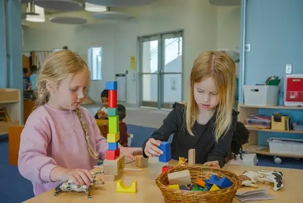 Students at St. Genevieve stack blocks and play with animal toys at a wooden Reach Table.