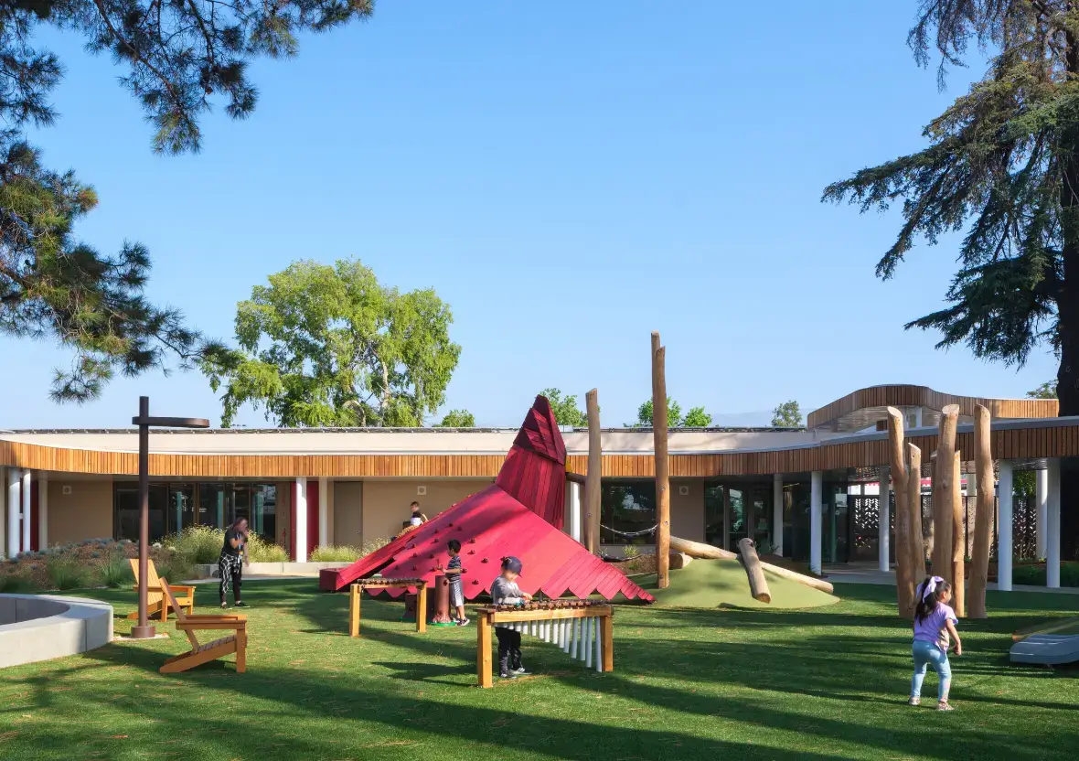 Children play on a striking red cardinal-shaped climbing structure, a focal point of the playground.
