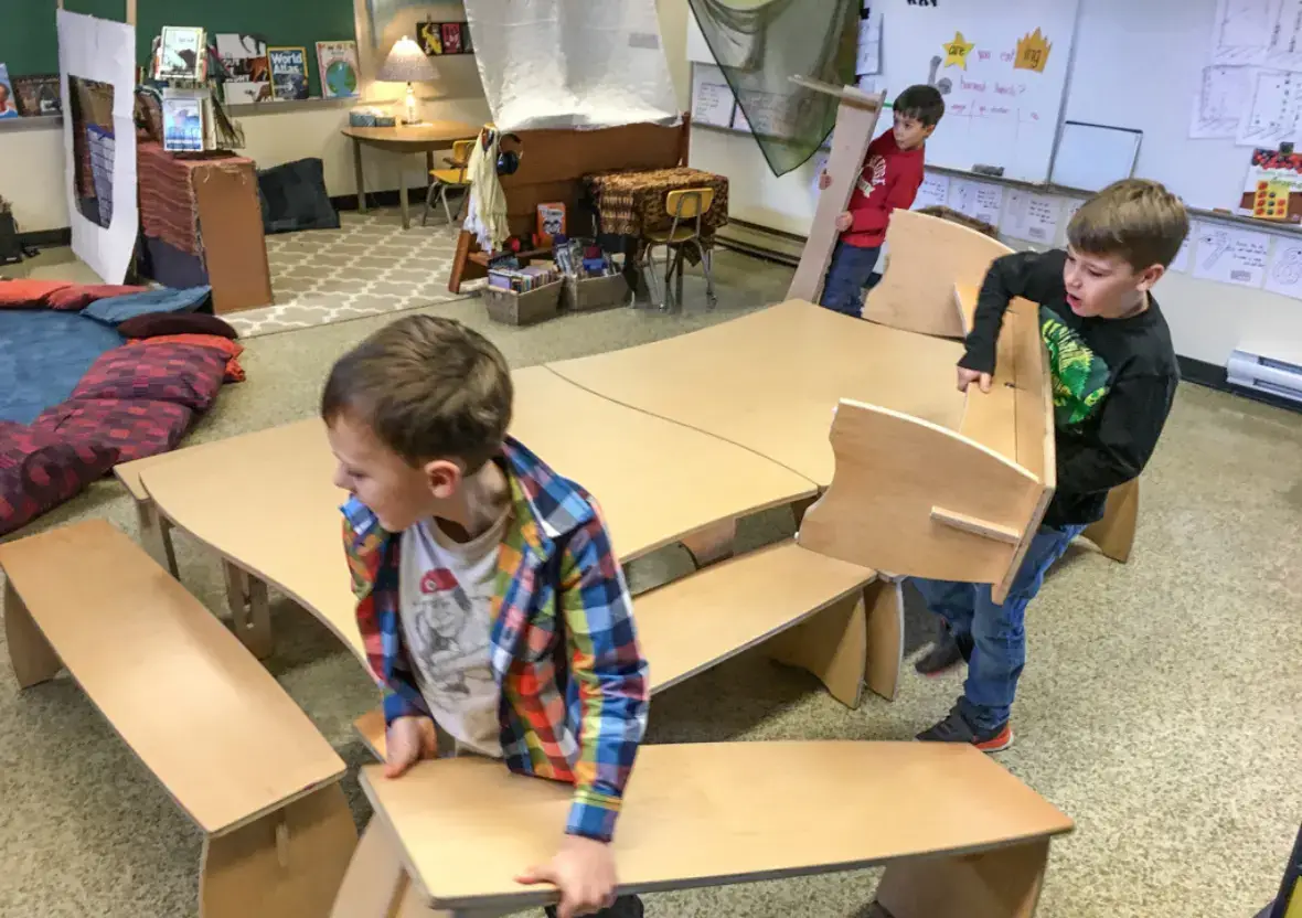 Three students actively rearranging Natural Pod Share Benches to customize their flexible classroom space.