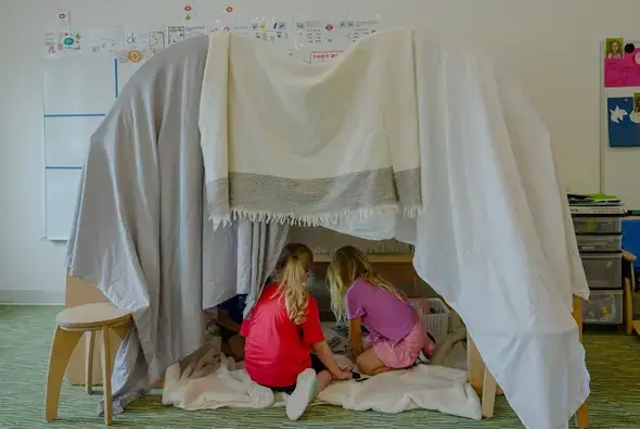 A creative fort made with fabric draped over Imagine Play Stands.