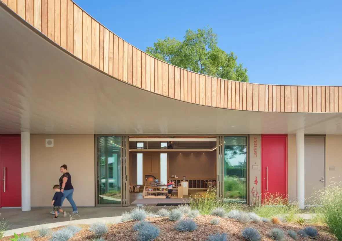 A family walks along an outdoor corridor toward an intentional design classroom with large sliding glass doors.