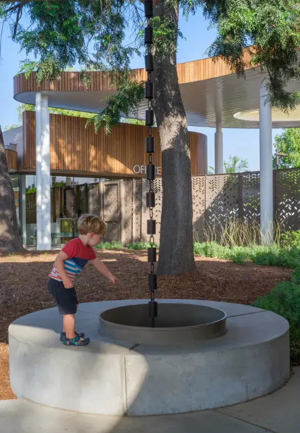 A young boy explores a metal rain chain, part of the center's outdoor sensory discovery. 