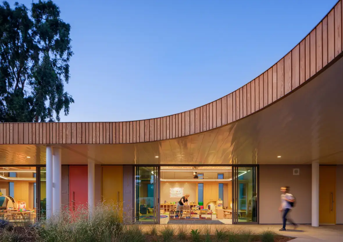 Modern learning environment exterior at dusk showing thoughtful lighting and a warm, glowing wood roofline.