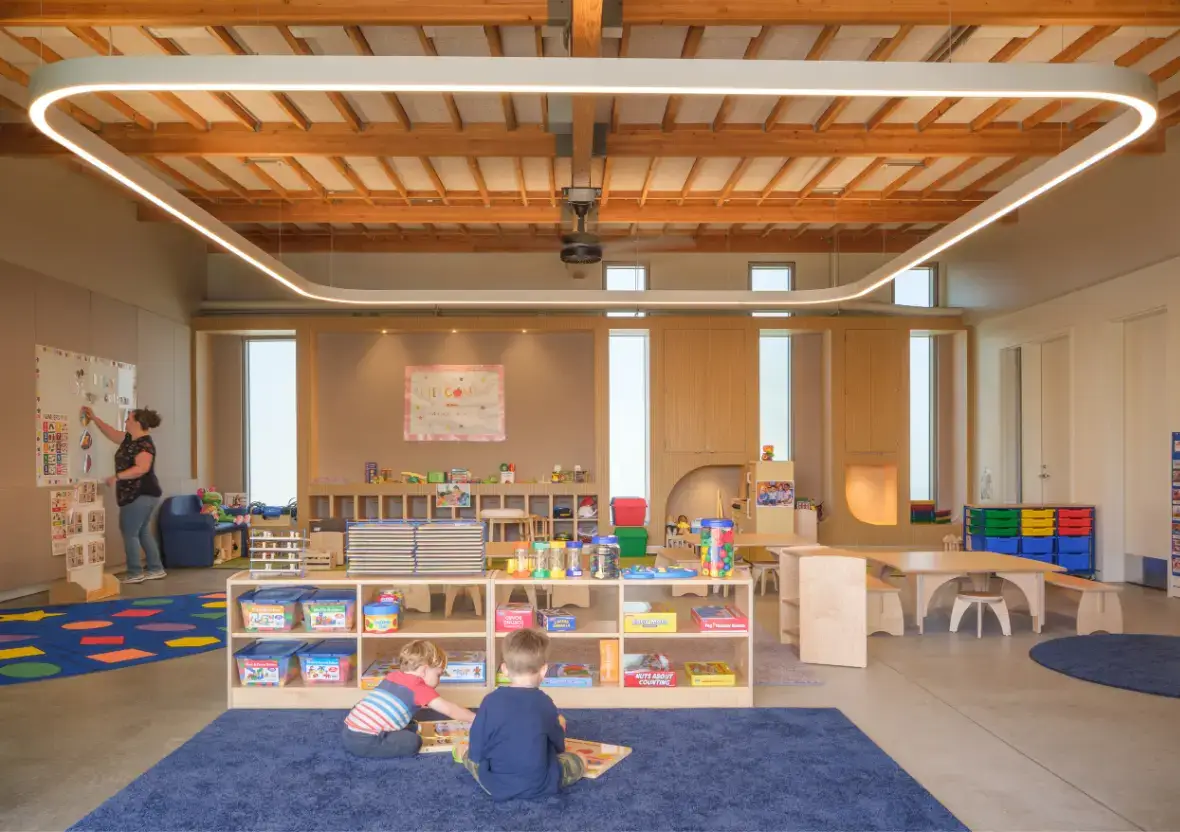 Early learning space embraces intentional design with low wooden shelving and an expansive halo light.