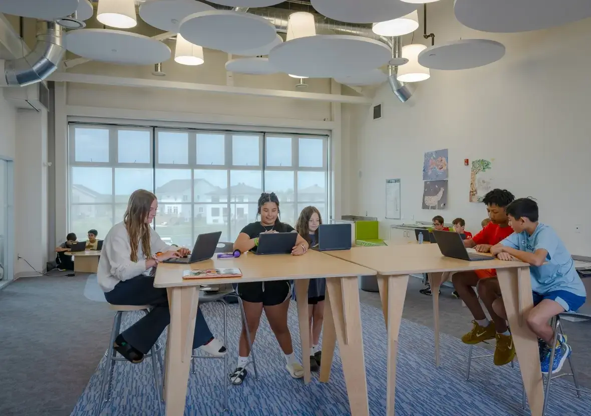 K-8 students collaborating on laptops at wooden Natural Pod Gather Tables, showcasing flexible learning space design at St. Geneviève Catholic School.