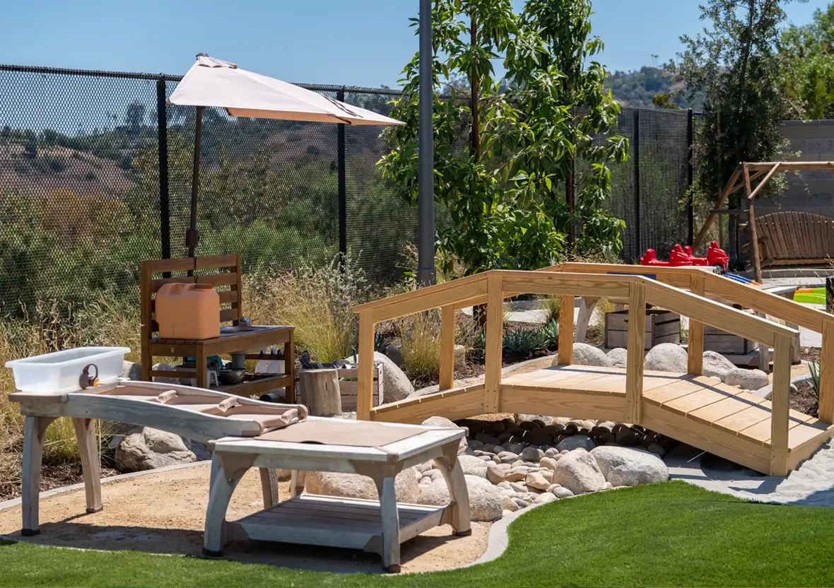 Outdoor play area with a wooden bridge, water play station, and sand pit for early learners.
