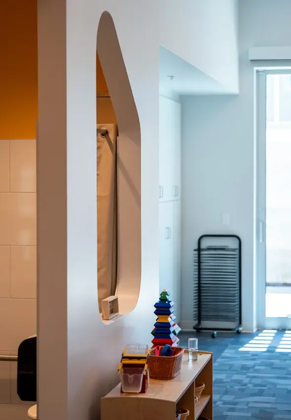 A light-filled room features the wooden Evergreen Shelving unit next to an architectural wall opening at the Thompson Family Center.
