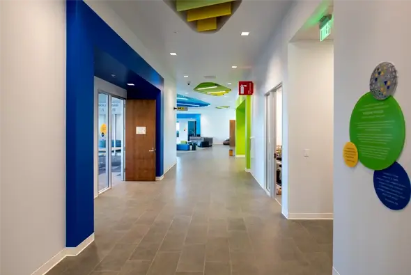 A long, brightly lit hallway in the Thompson Family Early Education Center with vibrant blue and green accent walls and modern lighting.