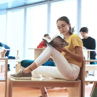 Middle-High-School-sq MIDDLE + HIGH SCHOOL: Student reading in a library while sitting on of Natural Pod's Evergreen Shelving which can also be used as seating.