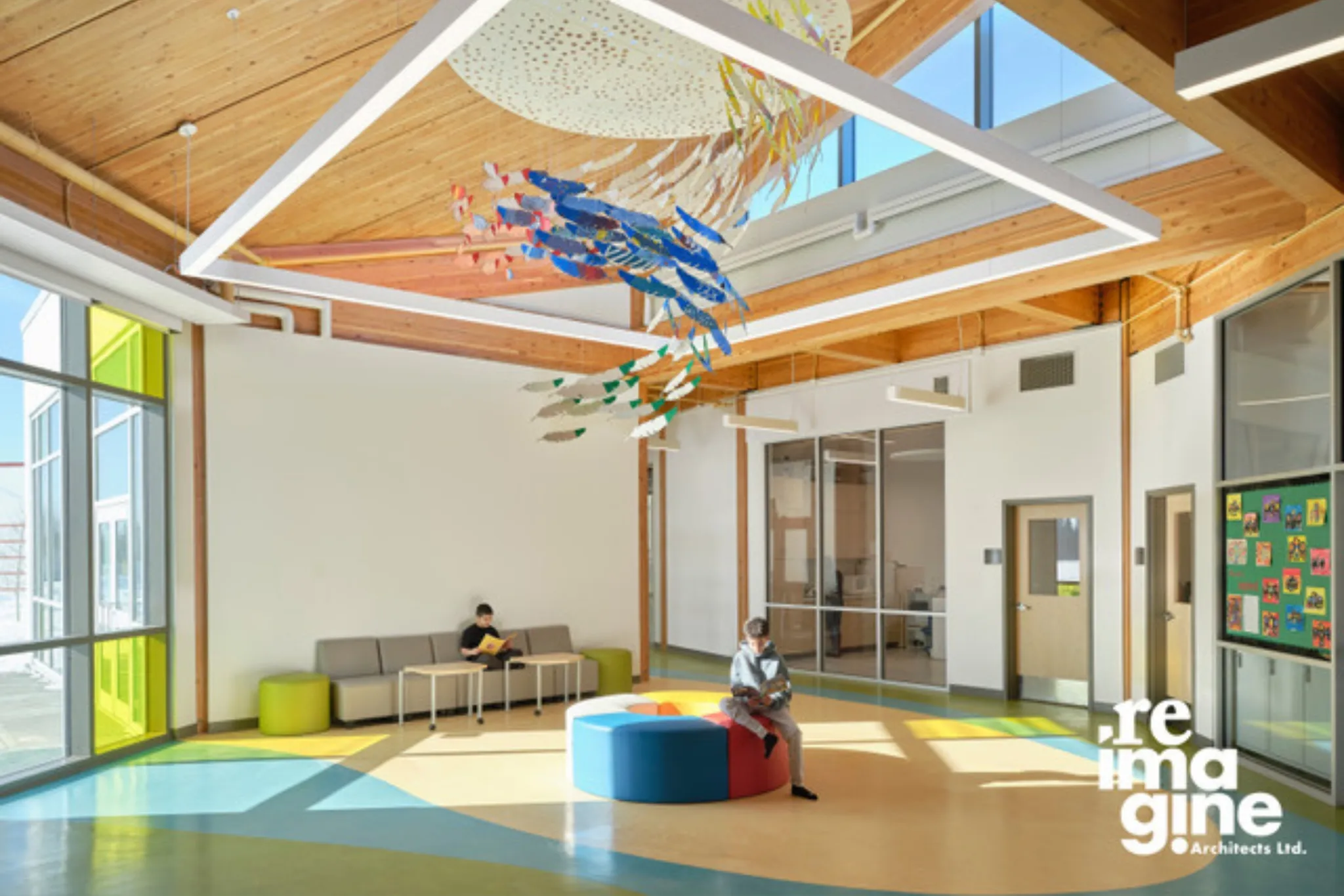 07-natural-pod-kipohtakaw-education-centre-common-area-1 Children relax in the spacious common area of Kipohtakaw Education Centre, featuring a colorful art display created by the students.