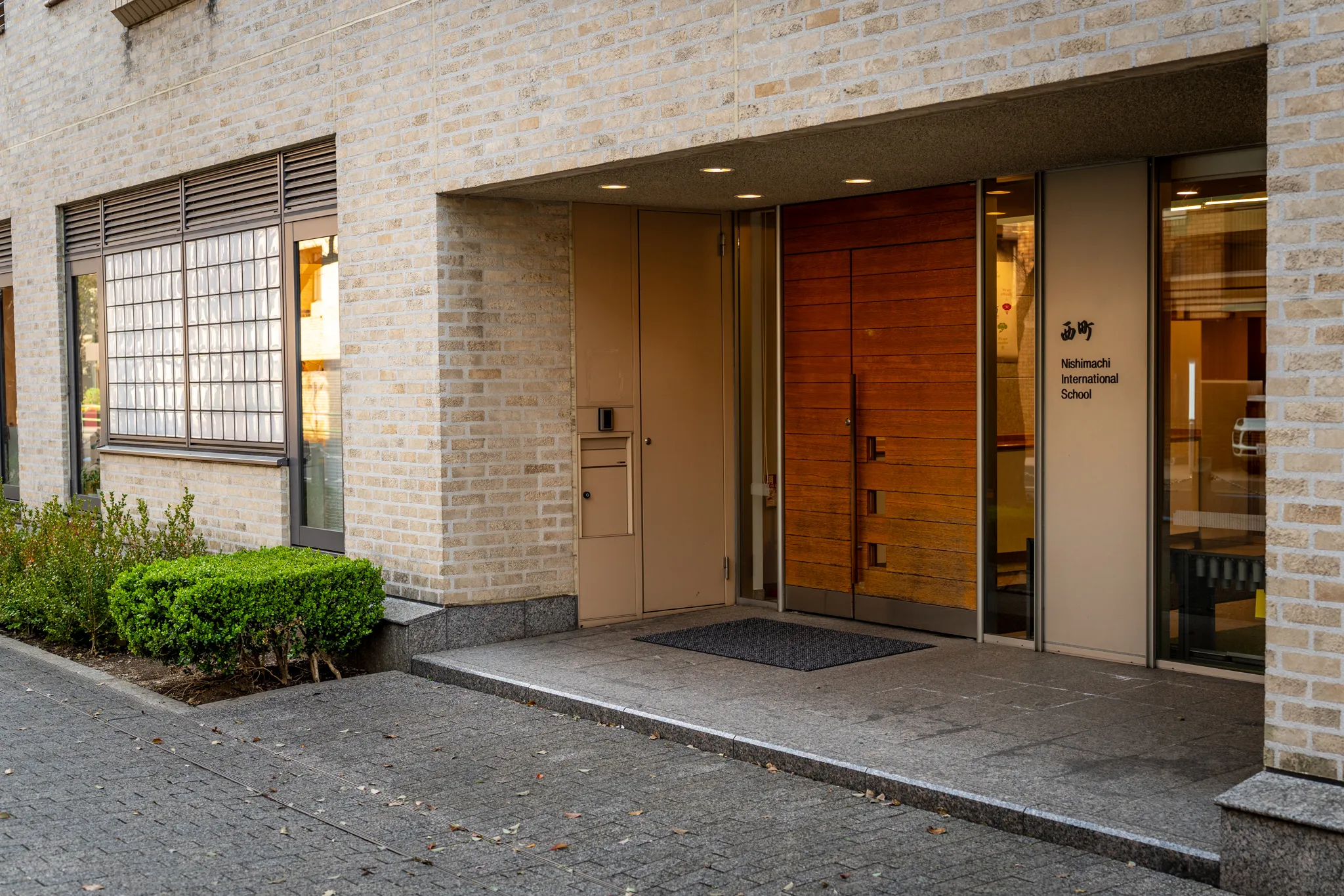 Front entrance of the Nishimachi International School building, showing modern brick architecture and wooden doors.